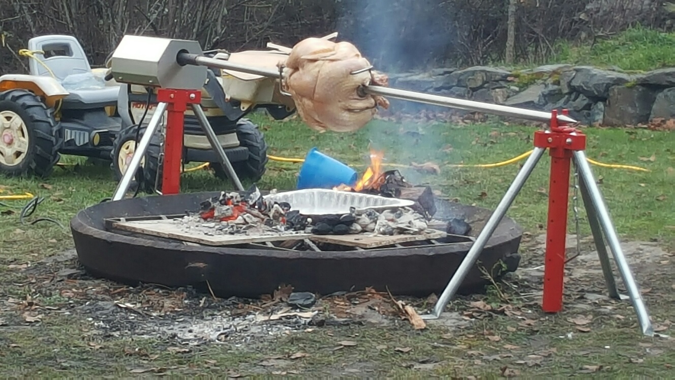 Poultry being cooked over an open flame outisde using a charcoal rotisserie