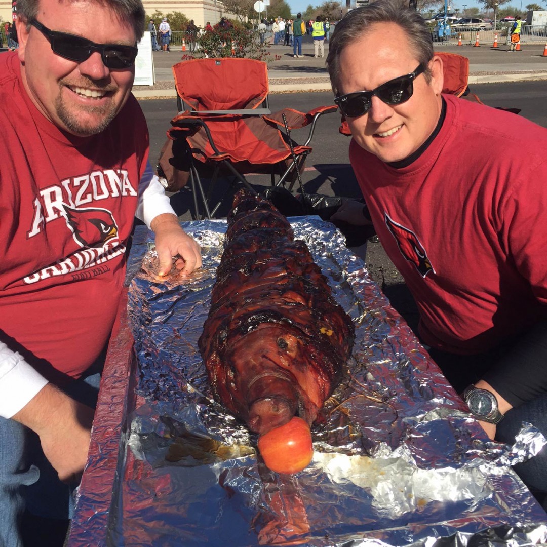 roasted pig on a large tin foil tray carried by two smiling men