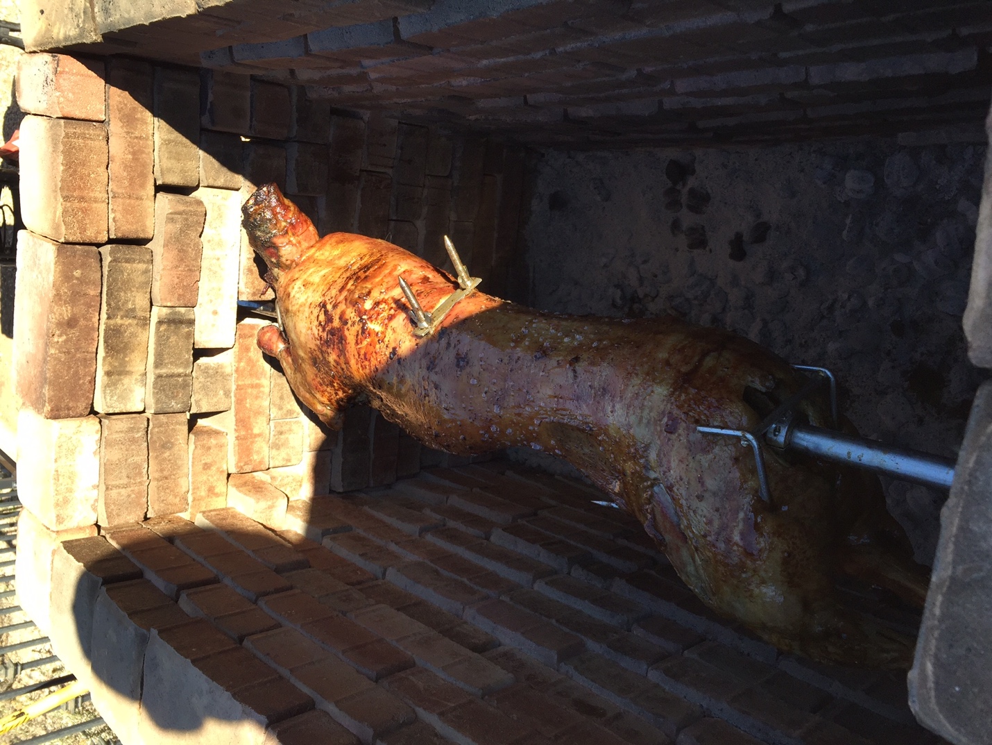 a cooked pig on charcoal rotisserie inside of a brick firepit