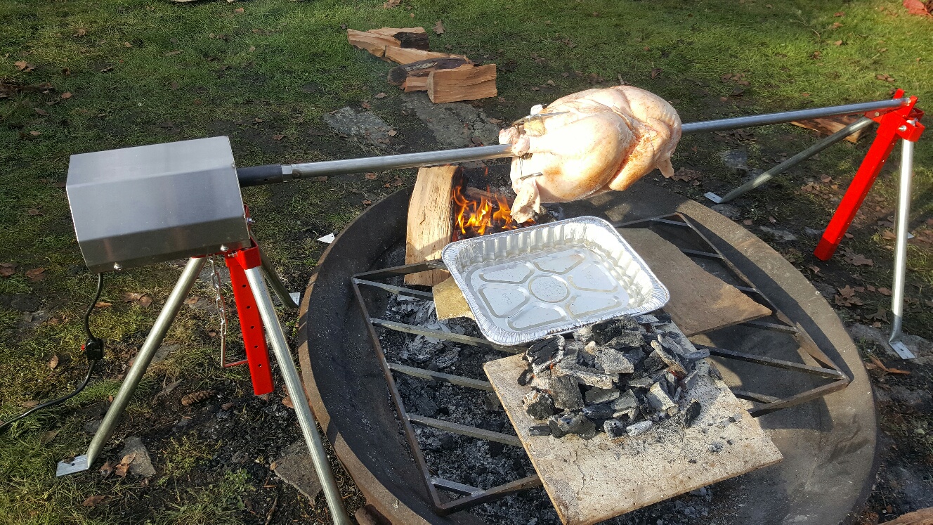 top down view of poultry being cooked over an open flame outisde using a charcoal rotisserie